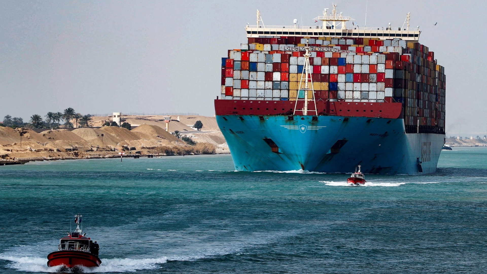 Front view of ship in water with coloured sea containers packed on deck